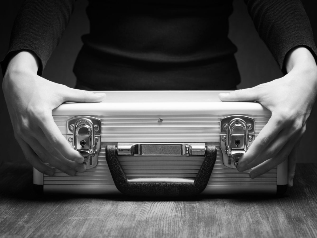 Close-up of a person holding a locked silver briefcase on a wooden table, symbolising secure cash courier services.