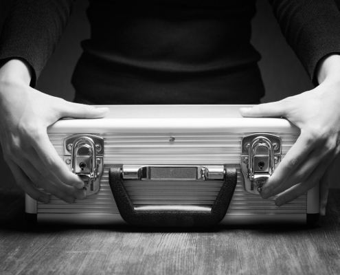 Close-up of a person holding a locked silver briefcase on a wooden table, symbolising secure cash courier services.