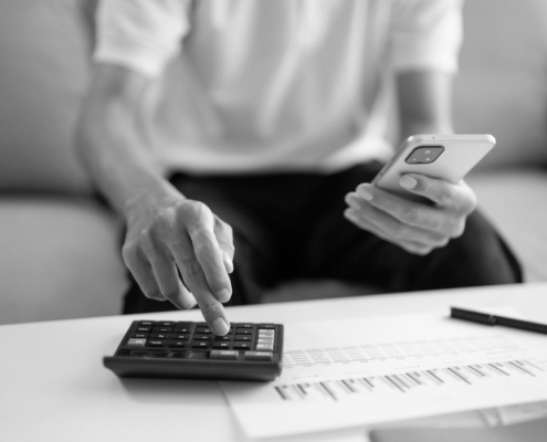 Person using a calculator and mobile phone while reviewing unpaid invoices and account paperwork related to business debt recovery.