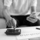 Person using a calculator and mobile phone while reviewing unpaid invoices and account paperwork related to business debt recovery.