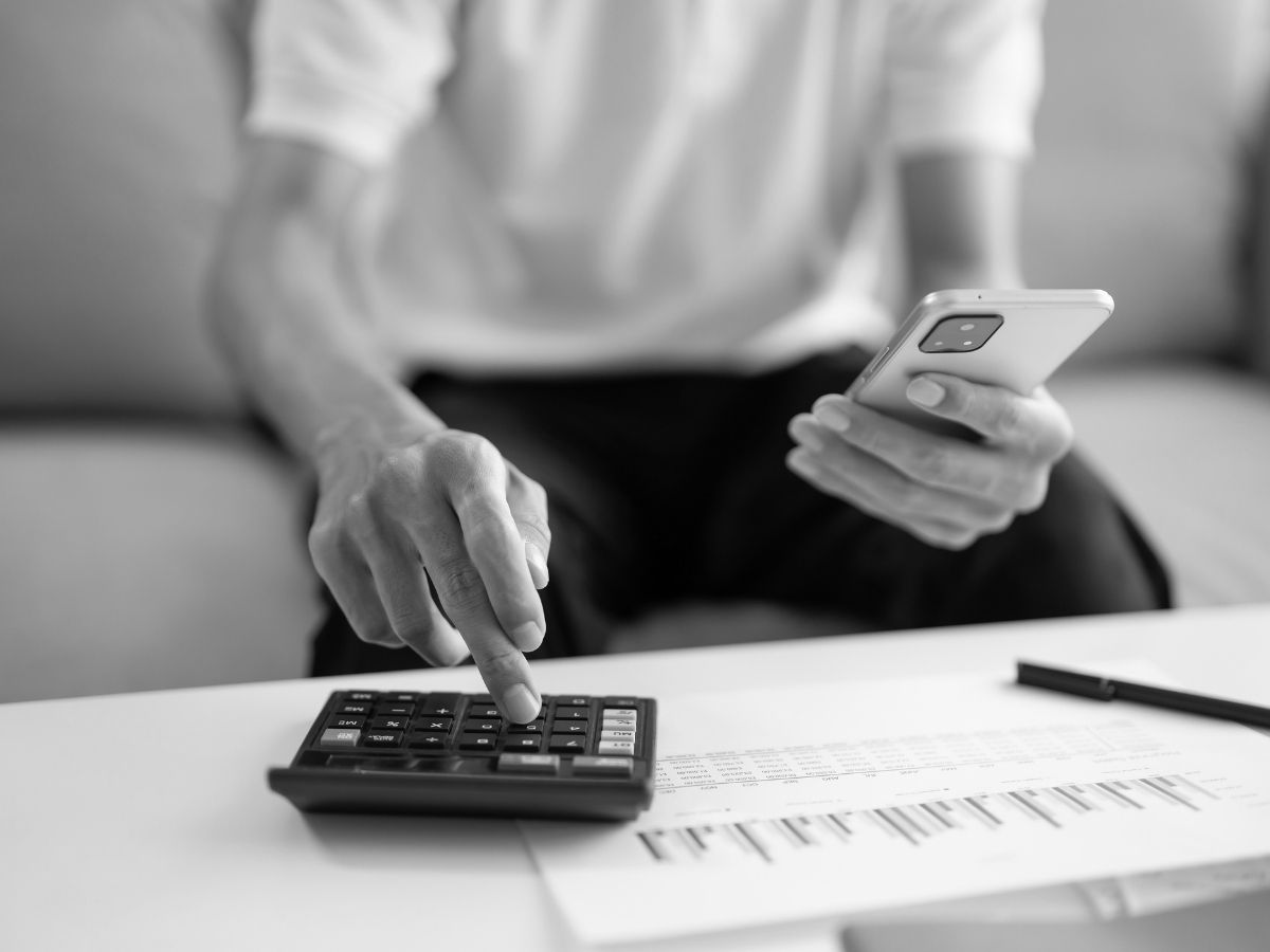 Person using a calculator and mobile phone while reviewing unpaid invoices and account paperwork related to business debt recovery.
