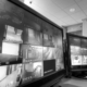 Security monitoring room with multiple CCTV screens displaying live camera views of business entrances, hallways and external areas.