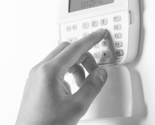 Person arming a business alarm system by pressing a code on a security keypad mounted on a wall