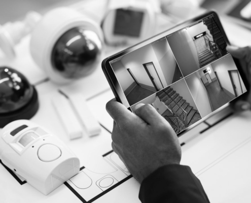 Person viewing live CCTV camera footage on a tablet, with security cameras and alarm sensors displayed on a building floor plan..